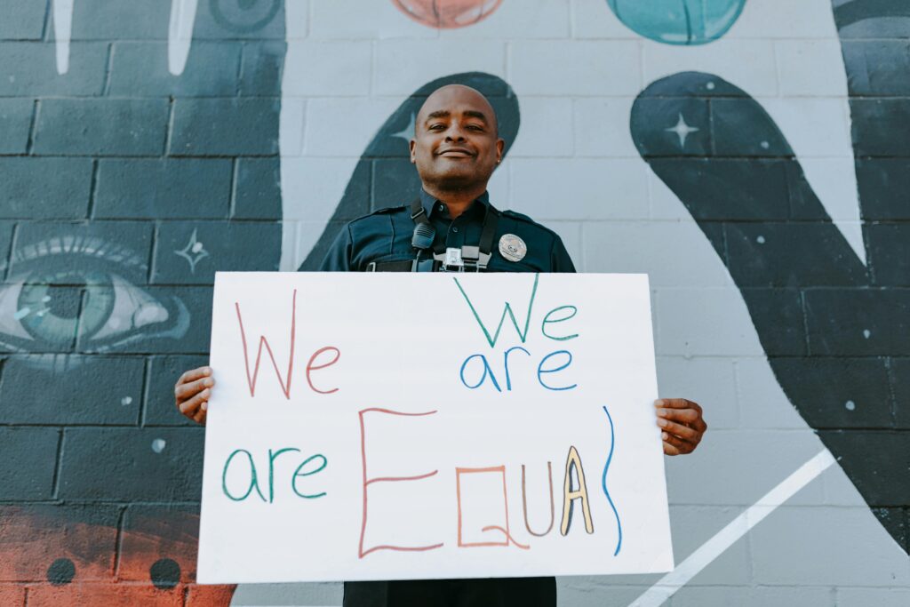A police officer stands with a 'We are Equal' sign, advocating equality.